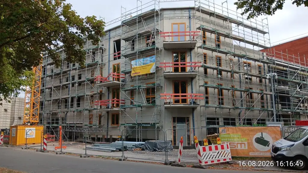 Rohbau eines Wohngebäudes mit Loggien und bereits eingesetzten Holzfenstern hinter dem Gerüst